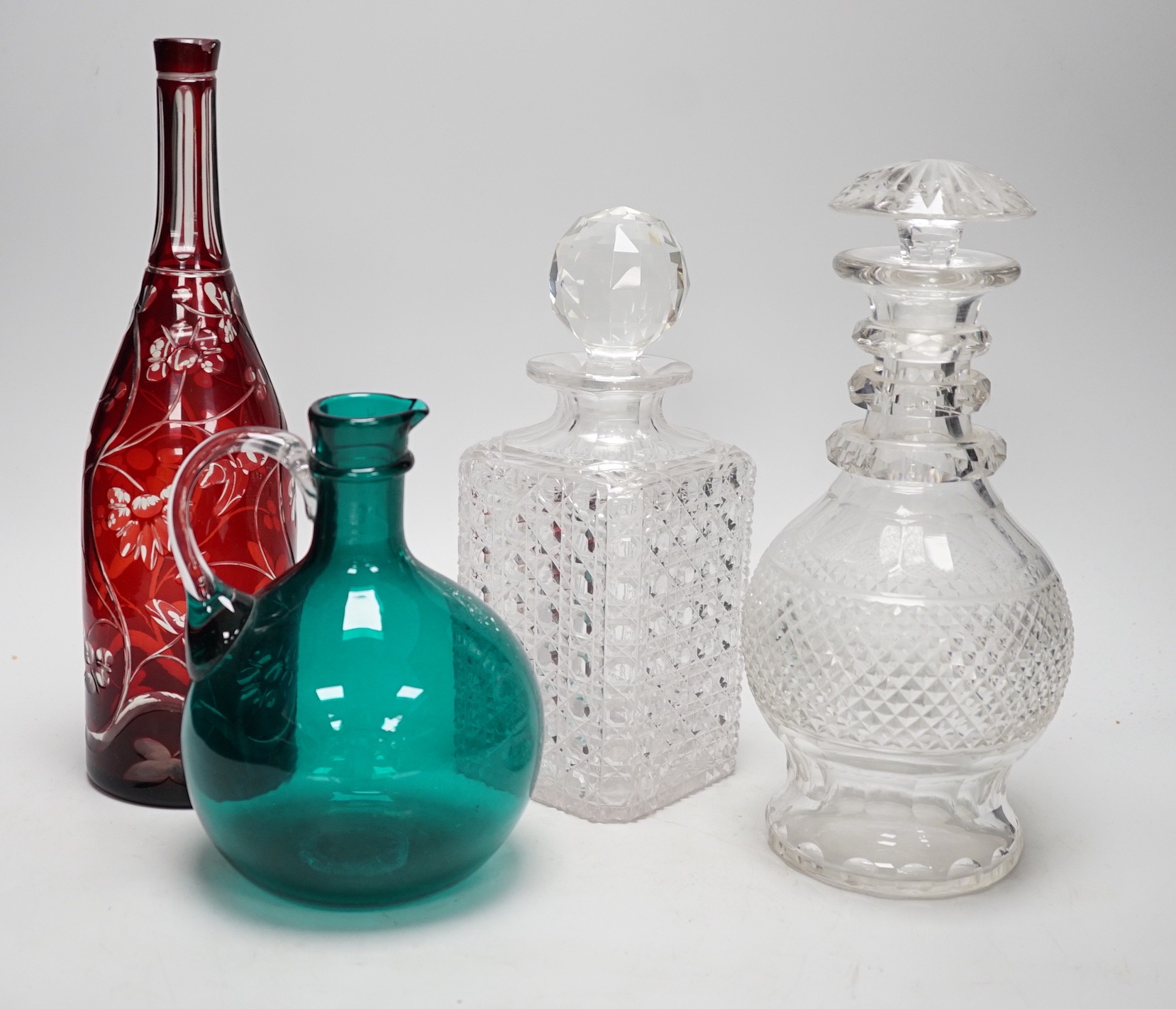 A green glass decanter flagon, a Bohemian red flash cut carafe (lacking stopper), a pineapple cut glass decanter and a square hobnail cut glass decanter (4). Tallest 30cm